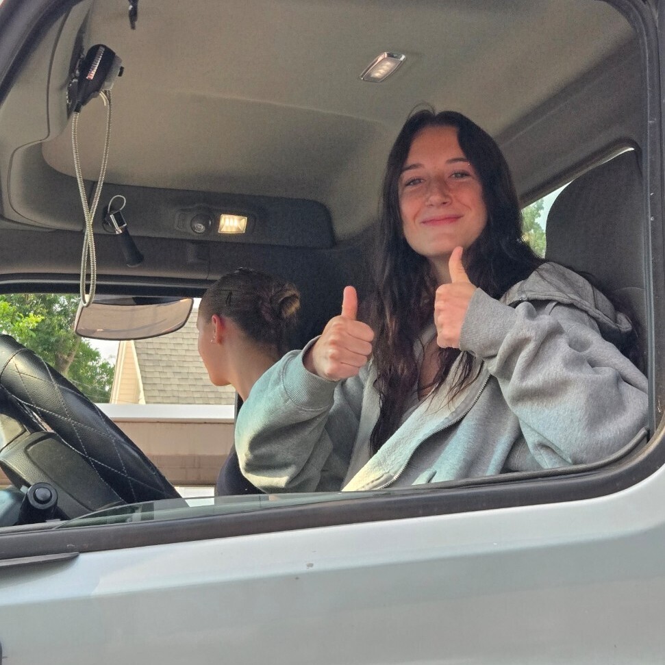 a female student sitting in a big rig truck poses with two thumbs up