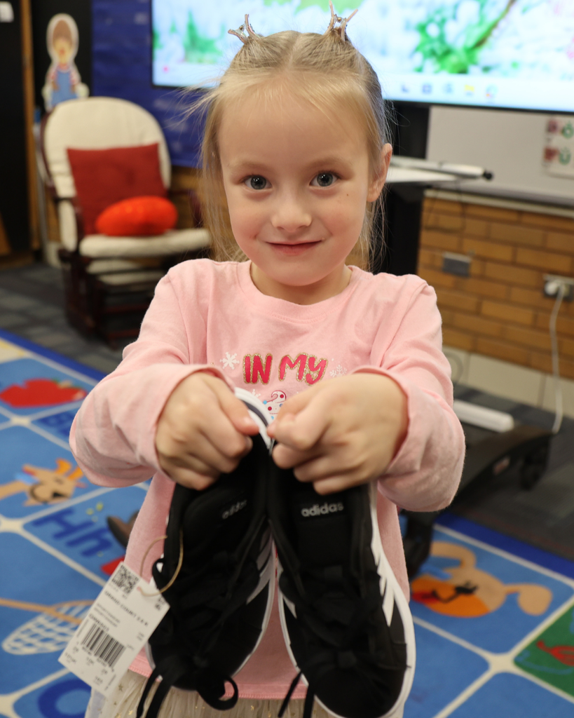 A student smiling while showing us a pair of shoes.