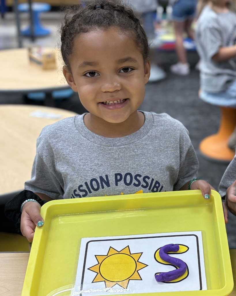 A student holding a tray that has an "s" made out of play dough in it.