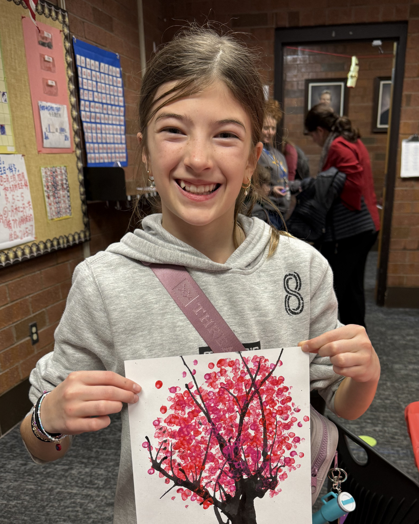A student smiling as they hold up their painting.