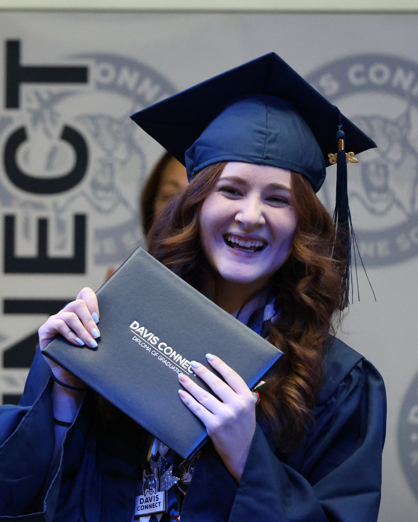 A Davis Connect graduate smiles while holding their diploma cover.