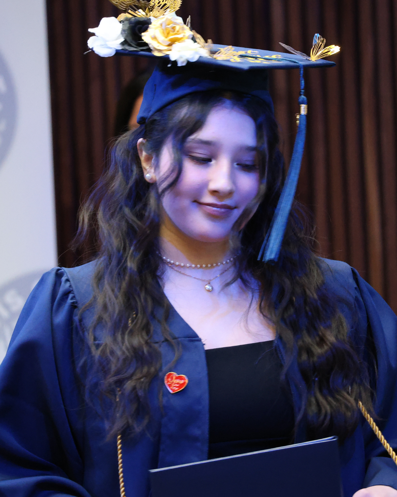 A Davis Connect Graduate wearing her cap that has gold butterflies on it, looks down.