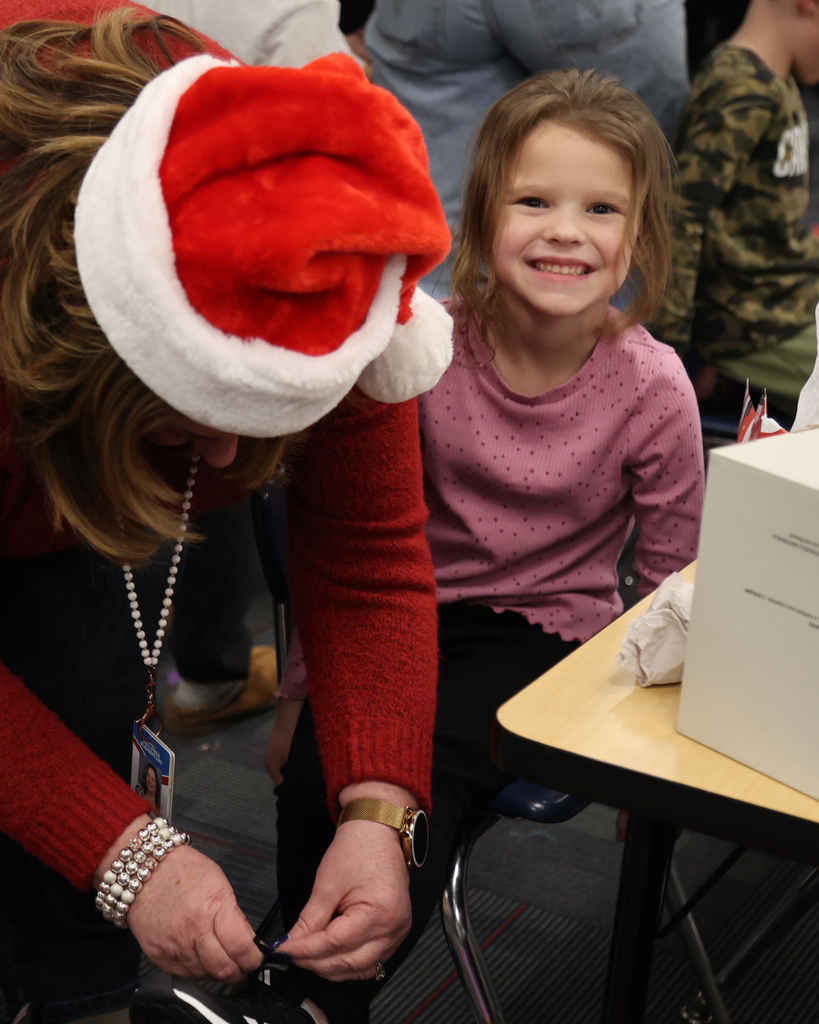 A student smiles while an adult ties her shoes.