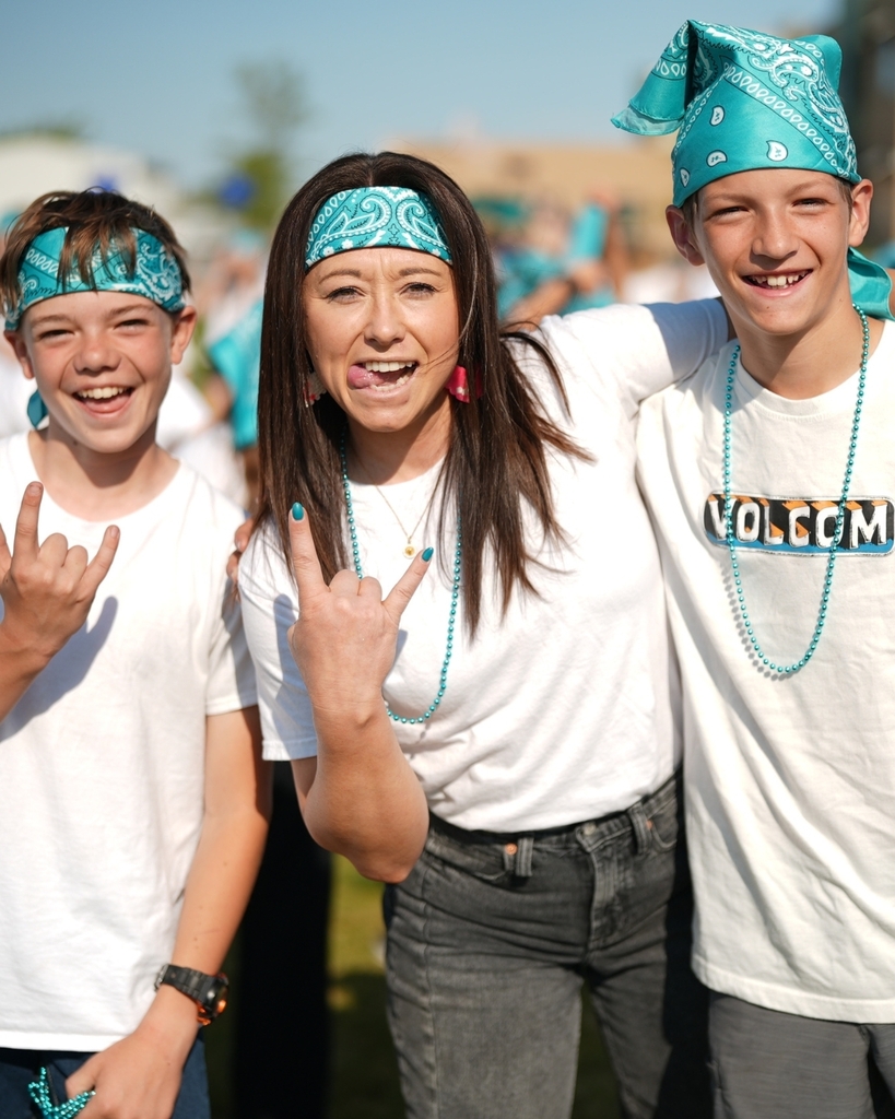 Two students and a teacher wearing blue bandanas smiling at the camera.