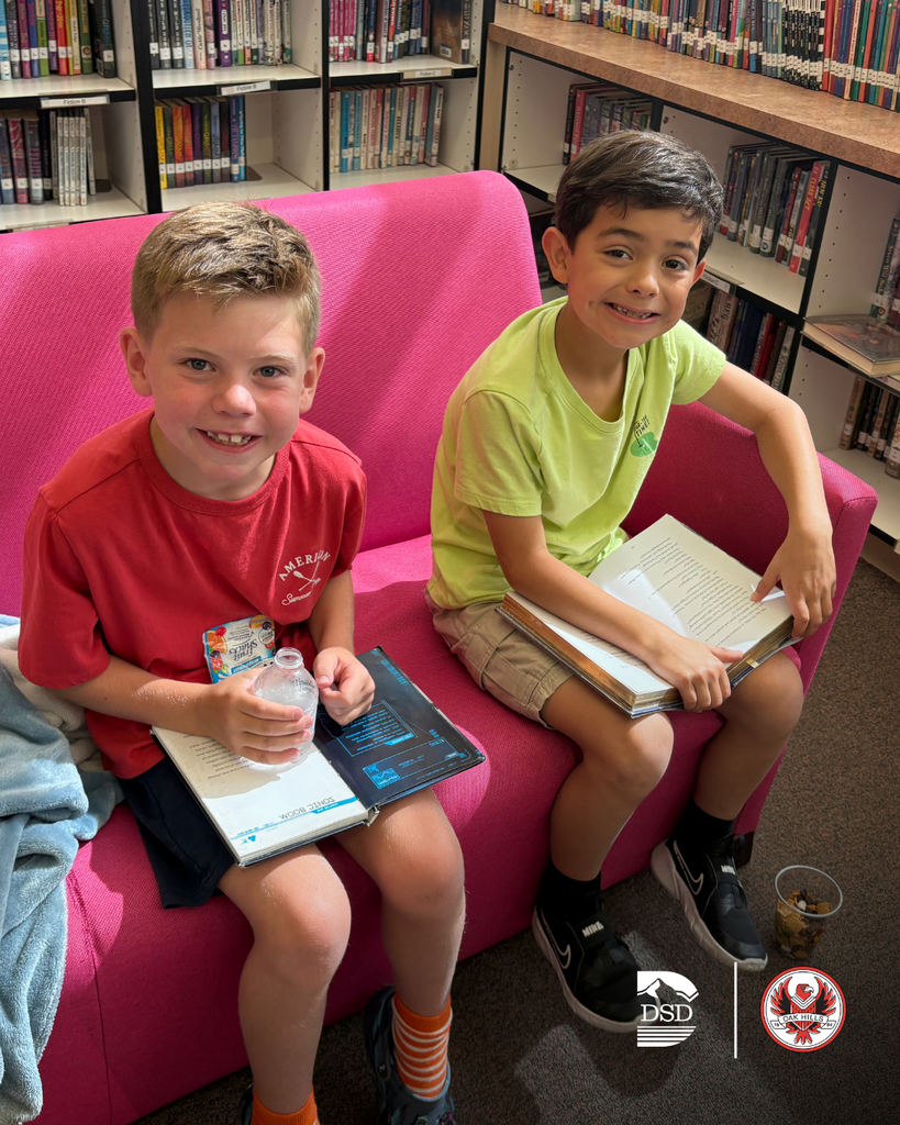 Students sitting on a pink couch reading.