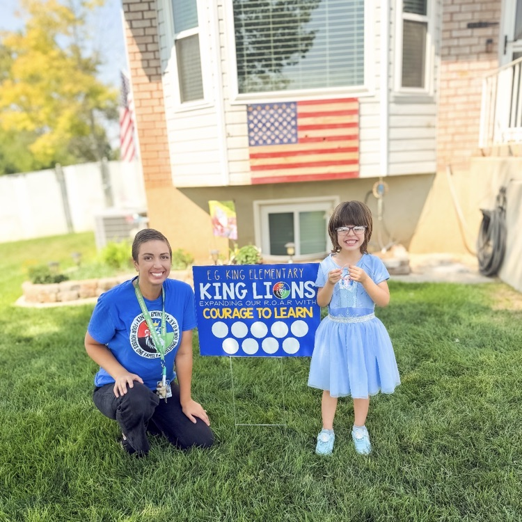 student and a teacher posing with school yard sign 