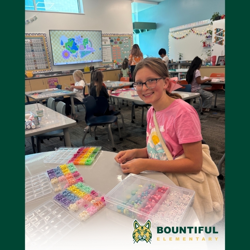 A Bountiful Elementary student smiles at a table filled with colorful beads and craft supplies during summer learning.