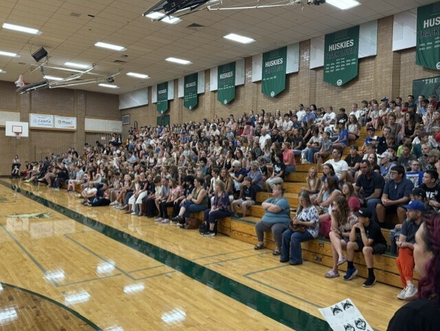 Students and families fill the gymnasium bleachers, waiting for Husky Camp to begin under green 'Huskies' banners