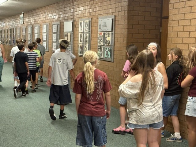 Students walk through a school hallway lined with photo displays during a school tour at Husky Camp.