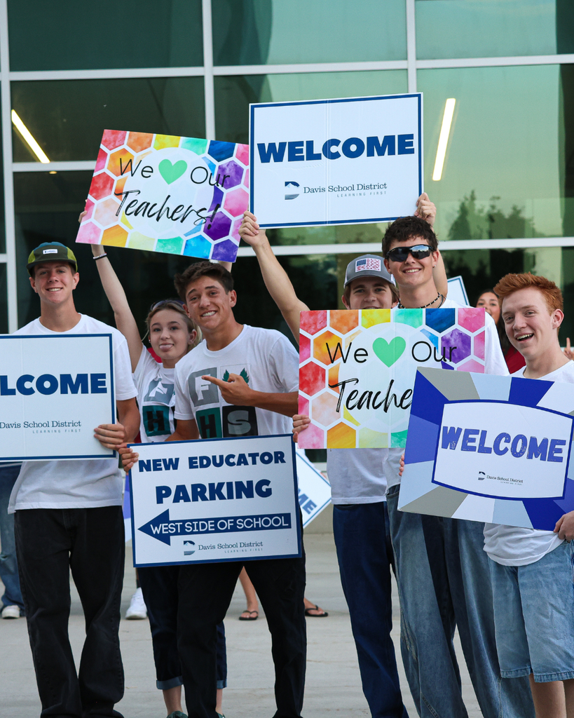 Students smile as they hold welcome and we love our teachers signs. 