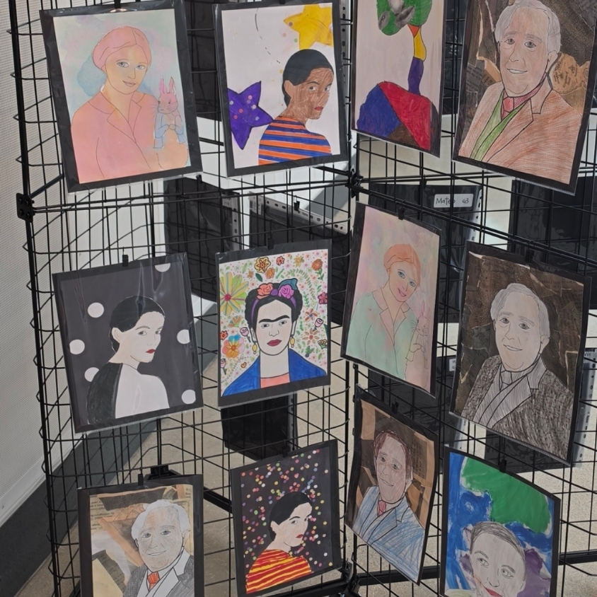 Close-up of a hallway art display showing student portraits clipped to black grid panels.
