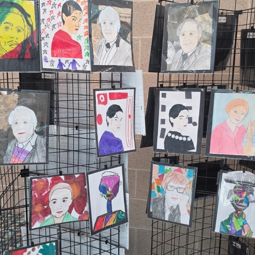 A school hallway display is filled with student-created portrait artwork in different colors, styles, and media.