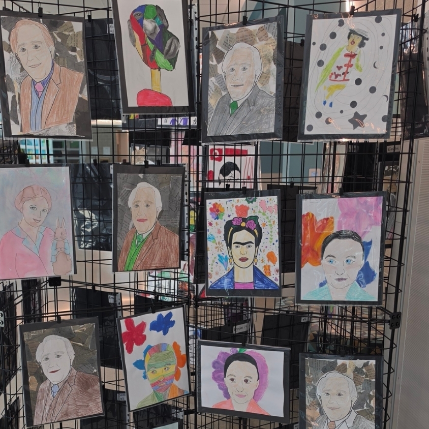 Student artwork featuring colorful portraits and mixed-media backgrounds is displayed on black hallway panels.