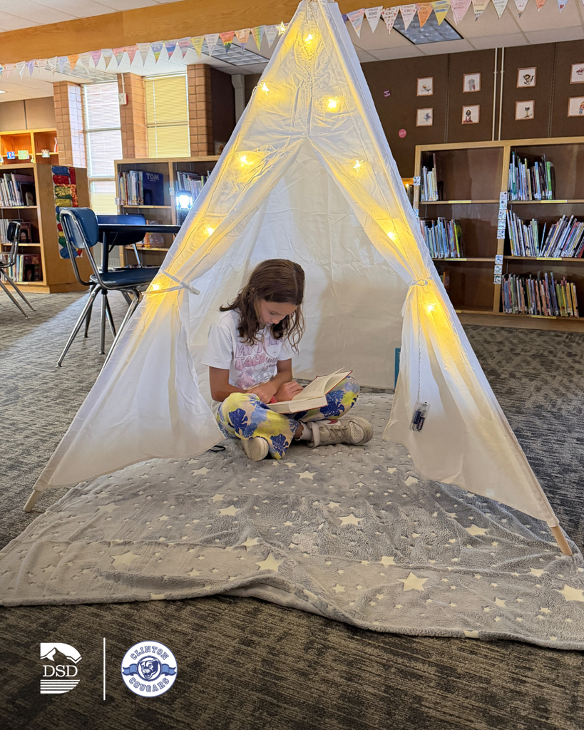 A student reading a book in a lit up tent inside.