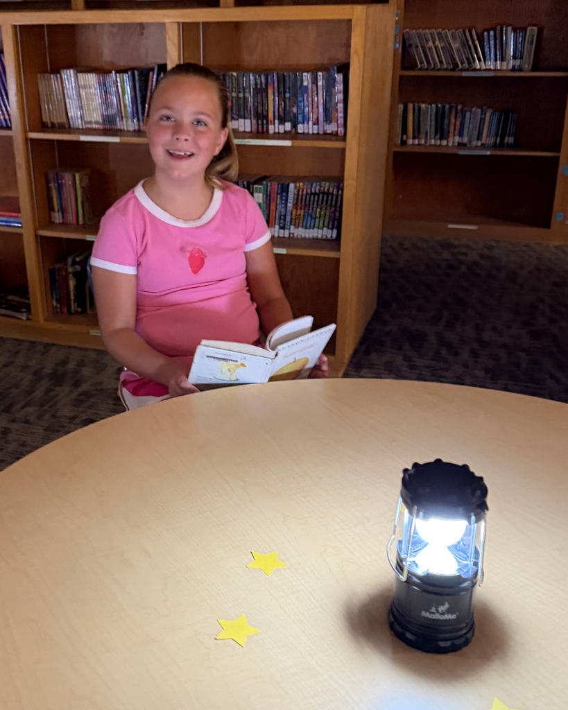 A student smiles as they read a book. They are illuminated by a lamp.