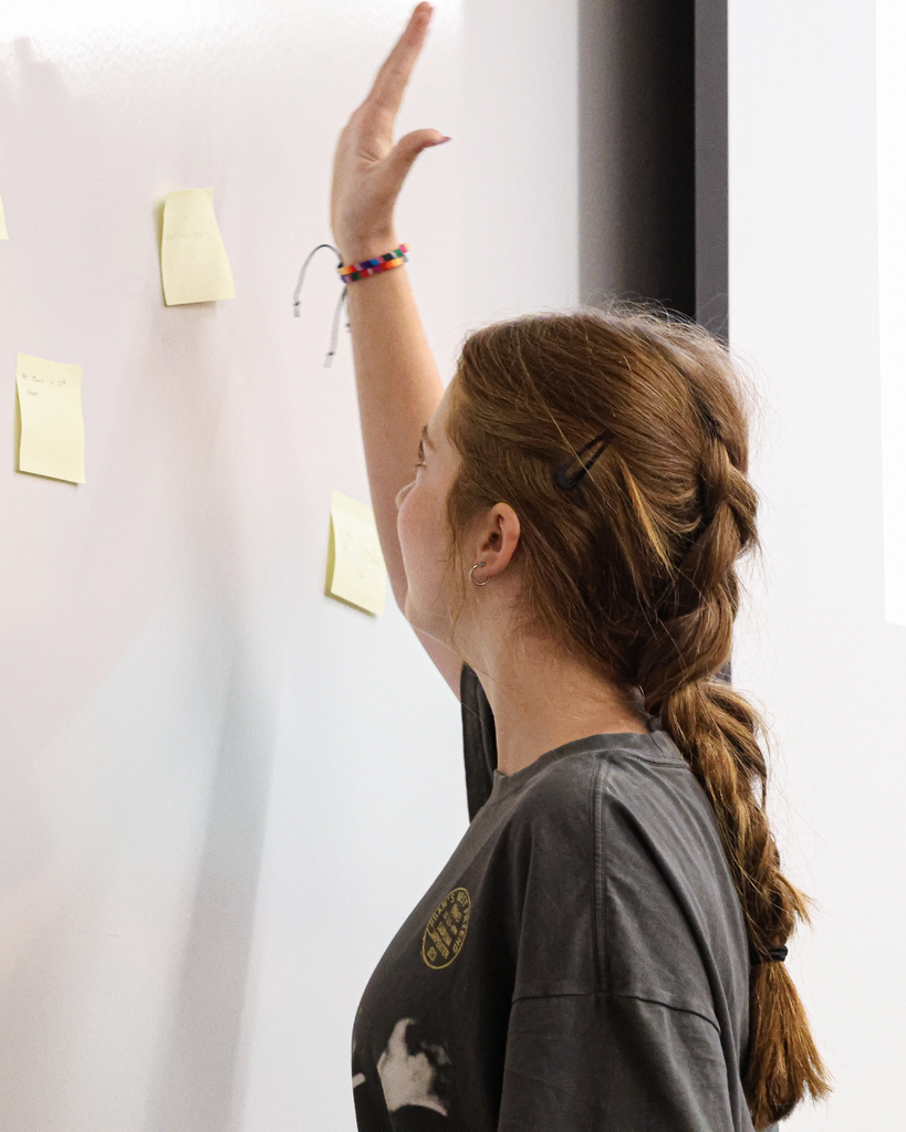 A student putting a sticky note on the white board.