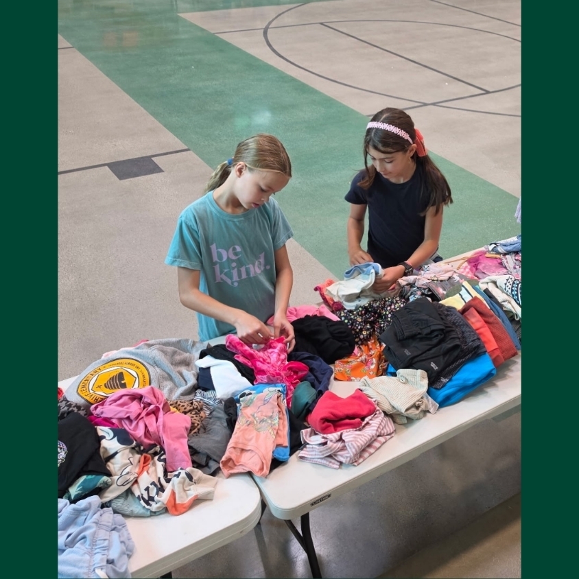 Two Hope Squad students sort and fold donated children’s clothing spread across tables in the Bountiful Elementary gym.