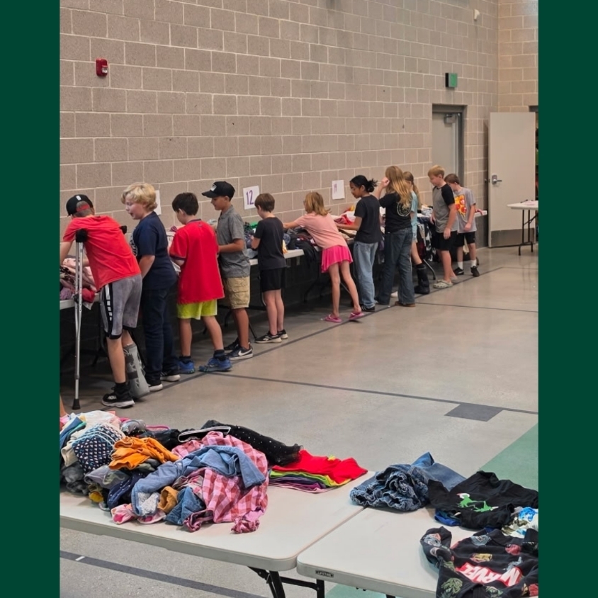 Hope Squad students work along a row of tables in the school gym, sorting large piles of donated clothing into organized sections by size.