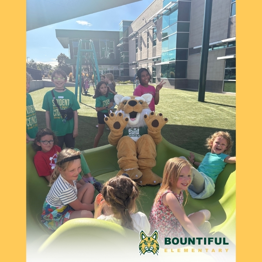 Bountiful Elementary students gather around the school’s Bobcat mascot on the outdoor playground during Back to School Night, with the school building in the background.