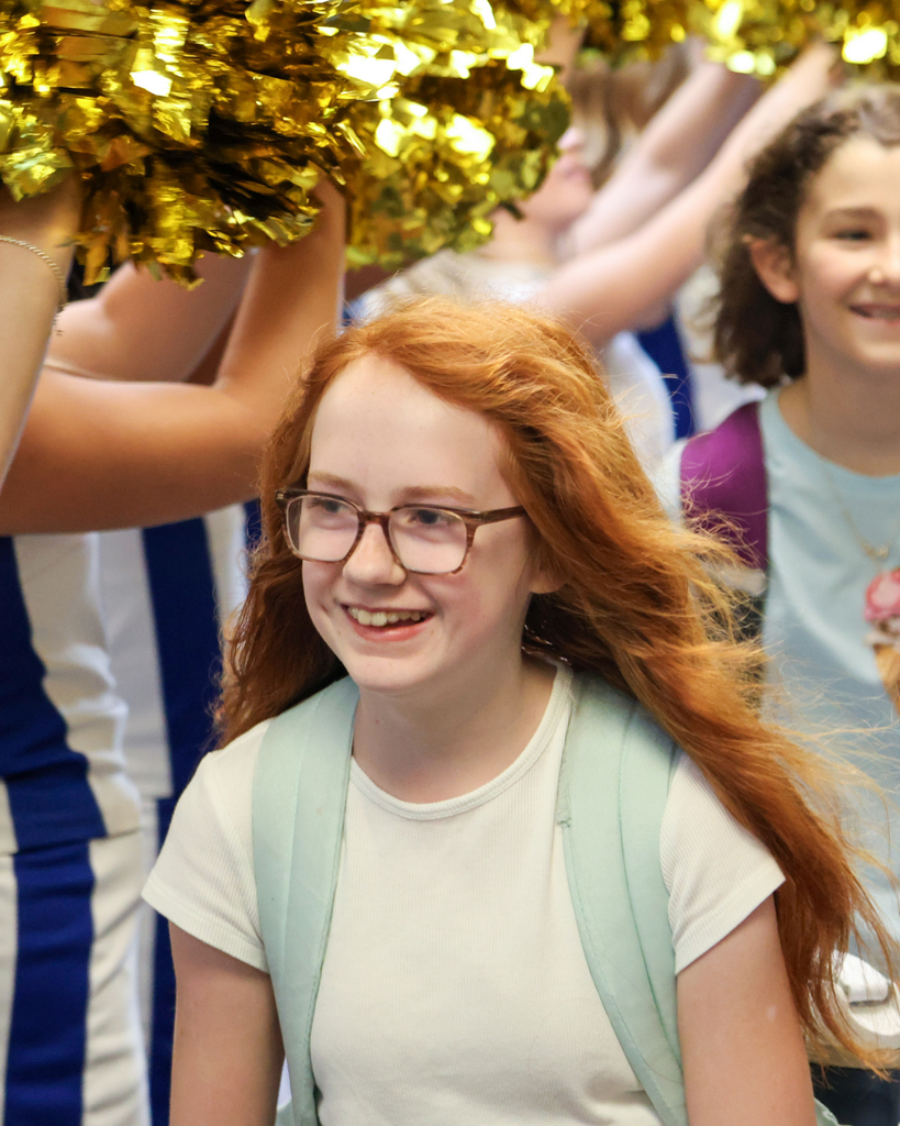 A student smiles as they enter the school with cheerleaders cheering.