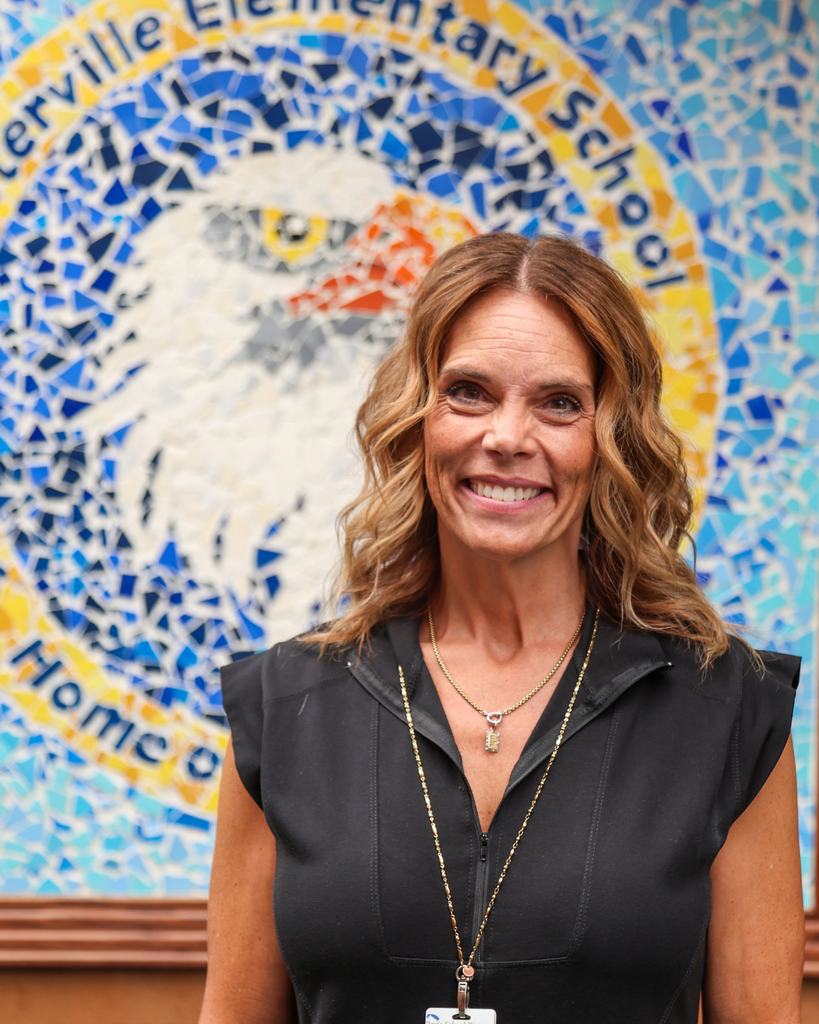 A principal smiling with a mosaic behind them.
