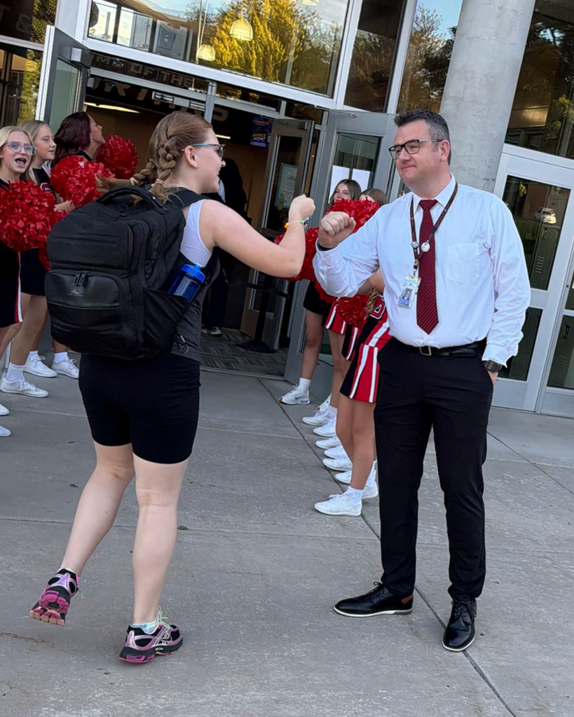 A principal fist bumping a student as they enter the building.