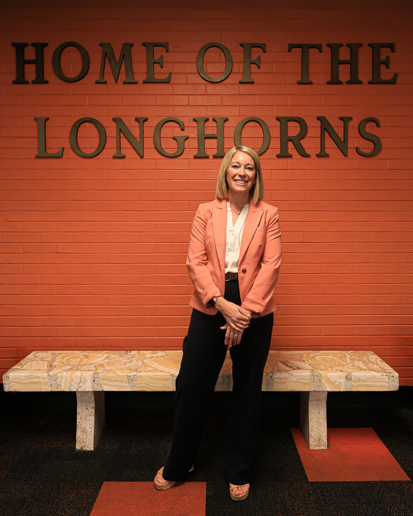 A principal standing in front of the words "Home of the Longhorns"