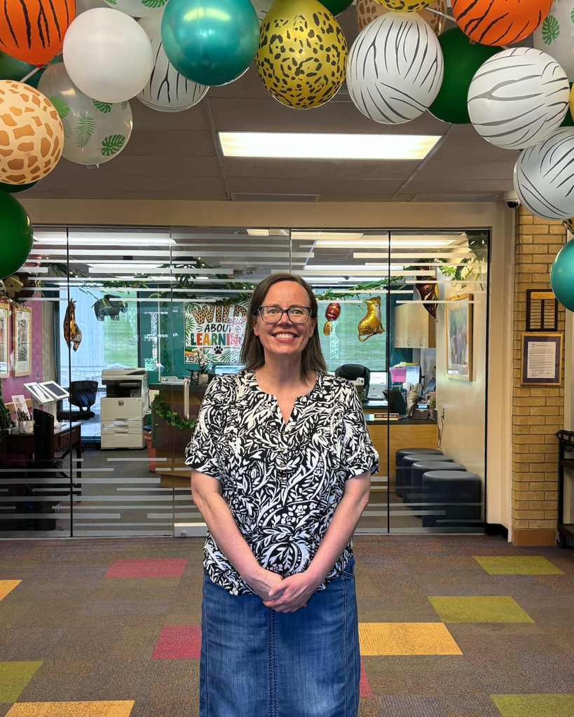 A principal smiling with a balloon arch.