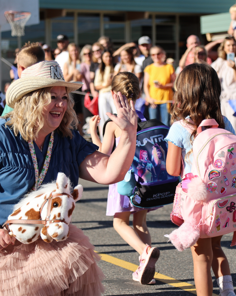 A principal wearing a hat high fives students.