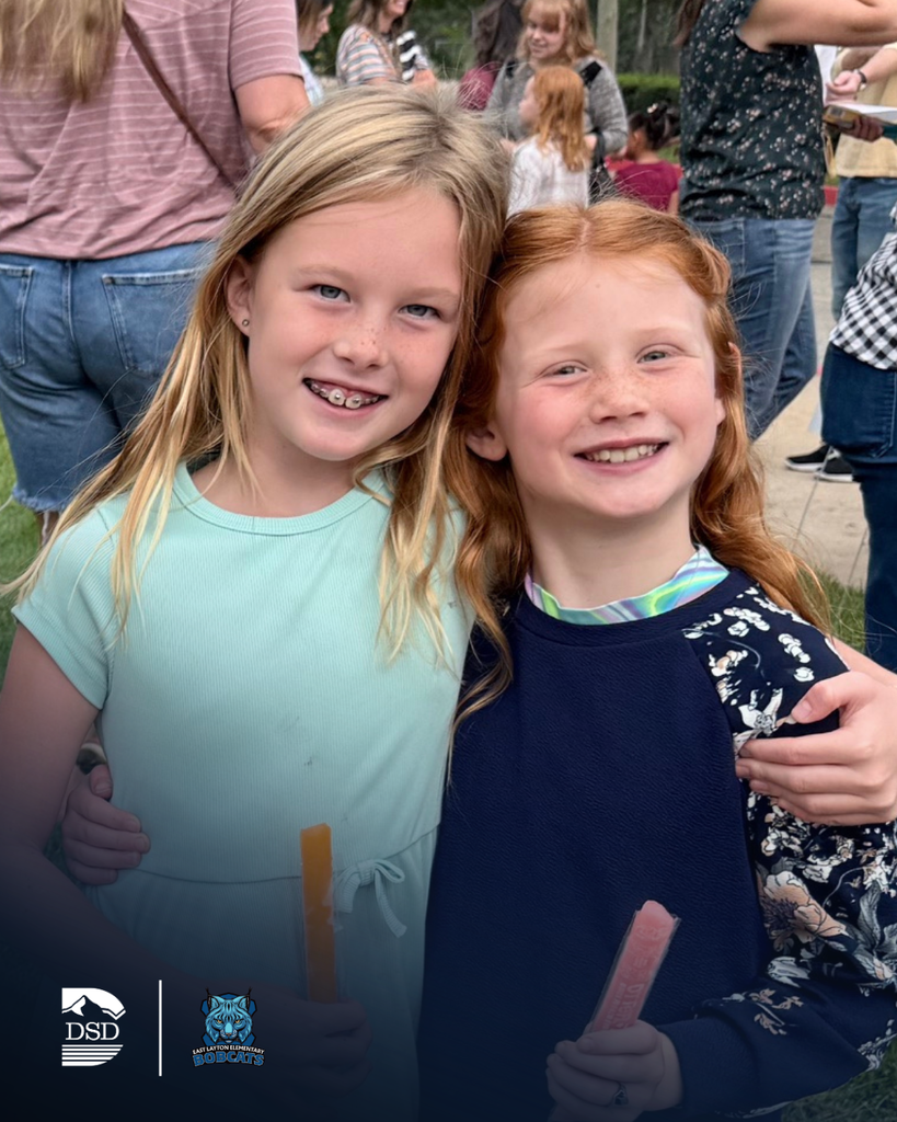 Two students hugging while holding popsicles.