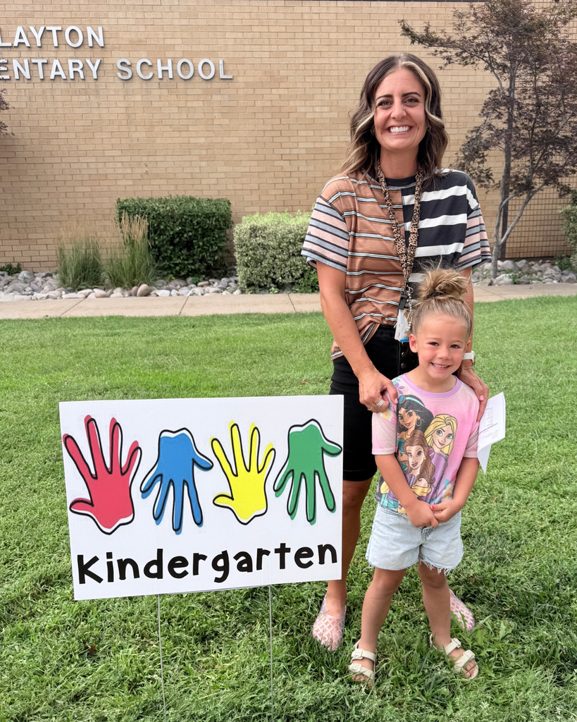 An adult and a student smiling as they stand next to a sign that says "kindergargen"