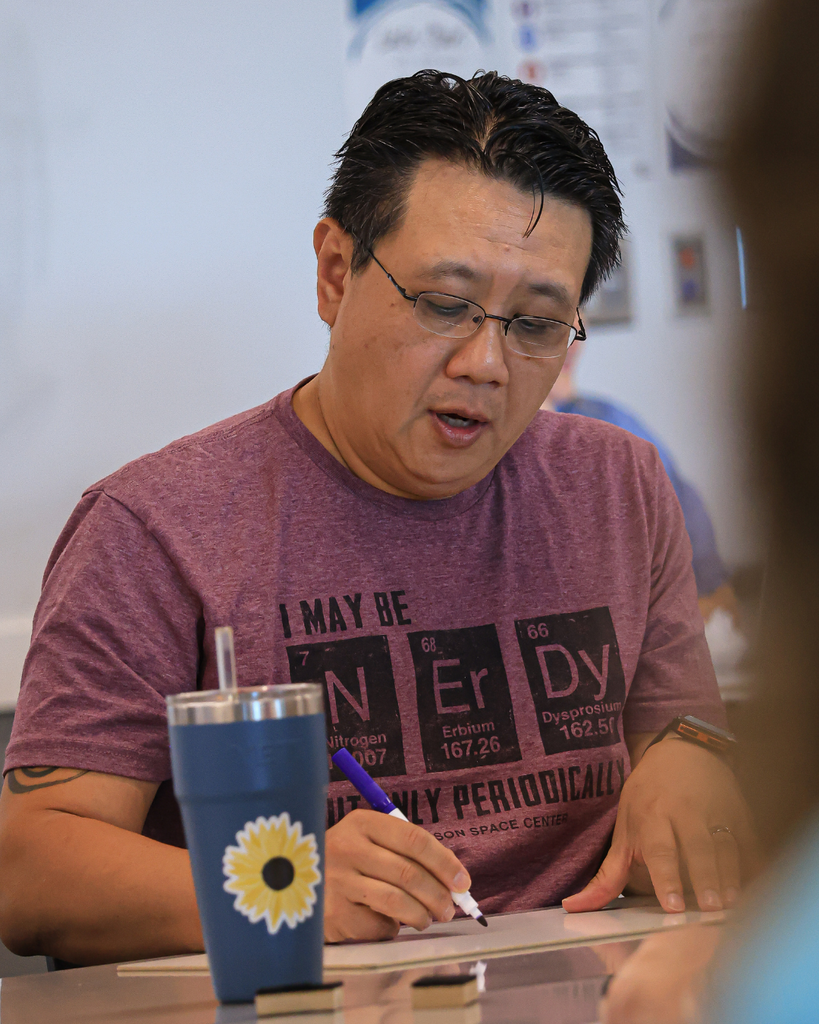 A teacher looks down as he writes on a white board.
