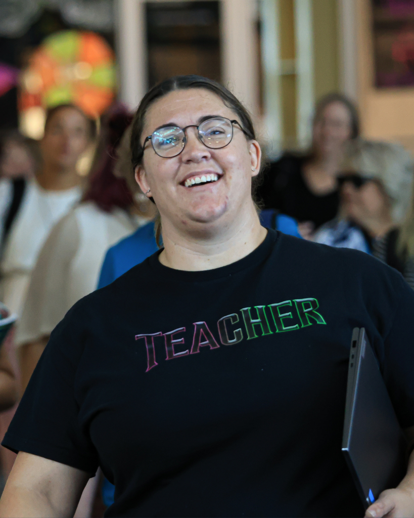 An adult wearing a shirt that says "teacher" smiles.