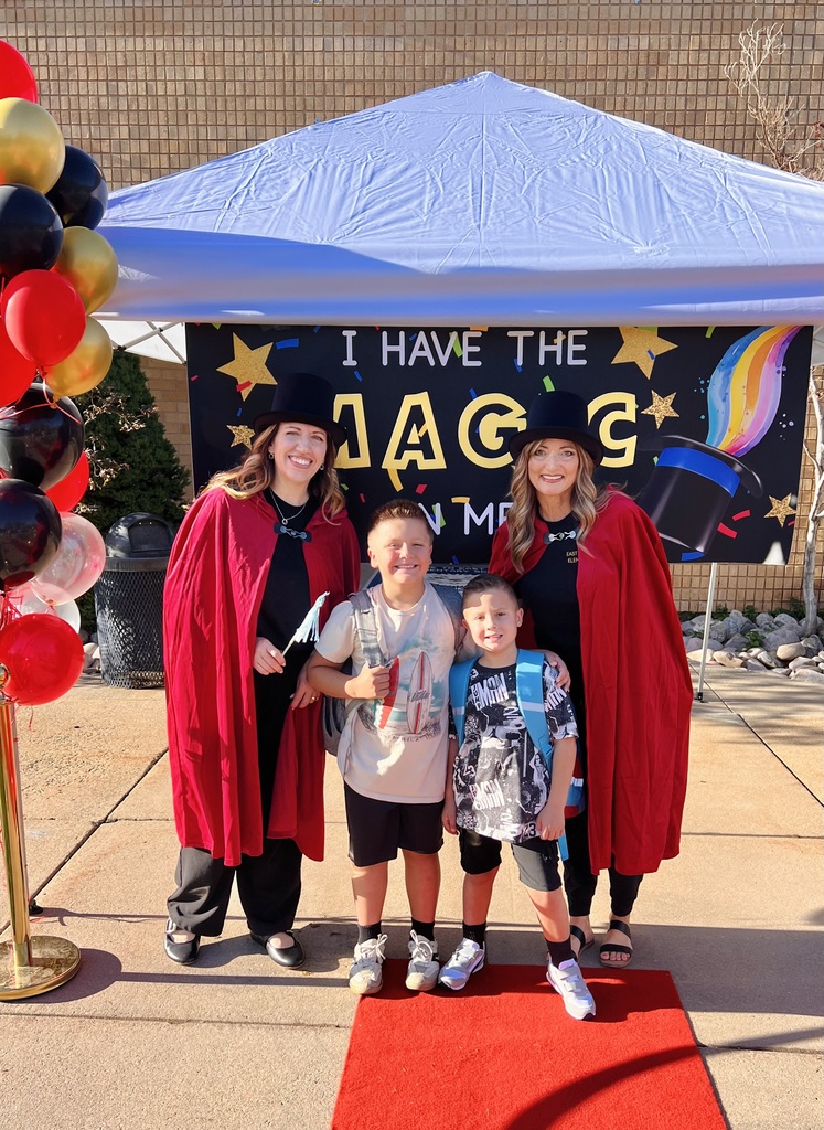 East Layton's Principal Murdock and Intern Summerhays in red bapes and black top hats standing in front of a sign that reads "I have the magic in me" with two students on the first day of school.