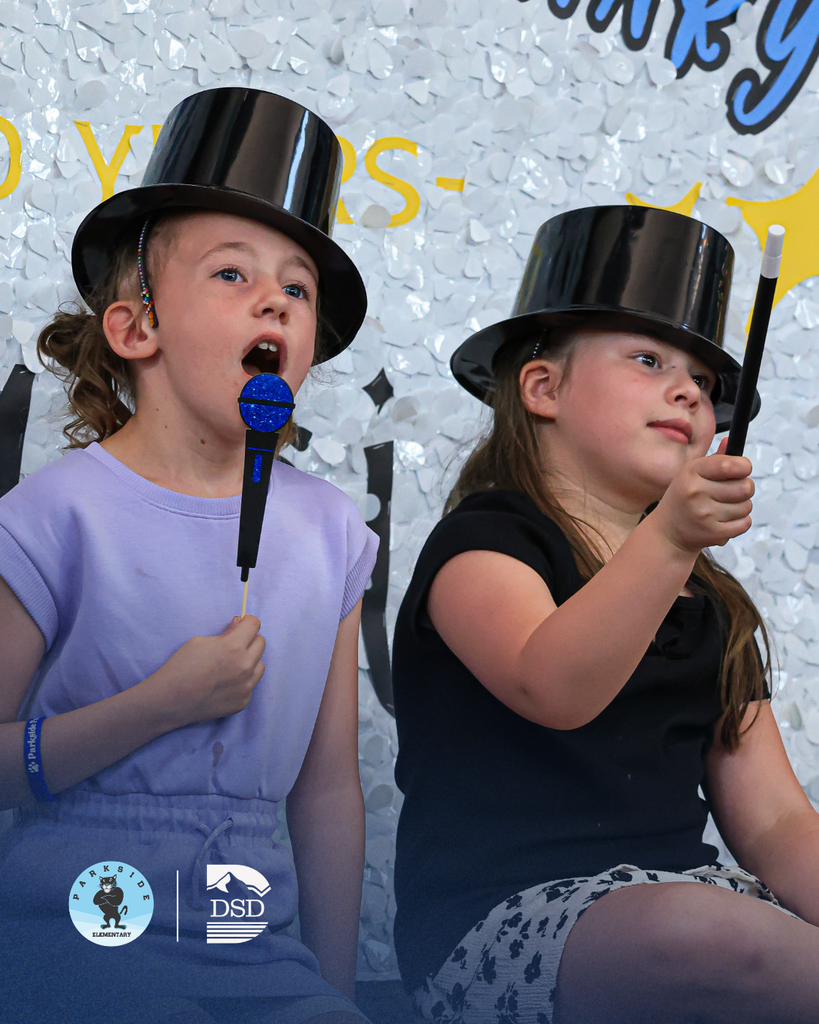 Two students sitting next to a confetti background wearing hats and holding photo props.