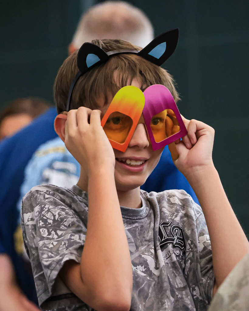 A student wearing panther ears and colorful popsicle glasses holds onto the glasses so they don't fall off.