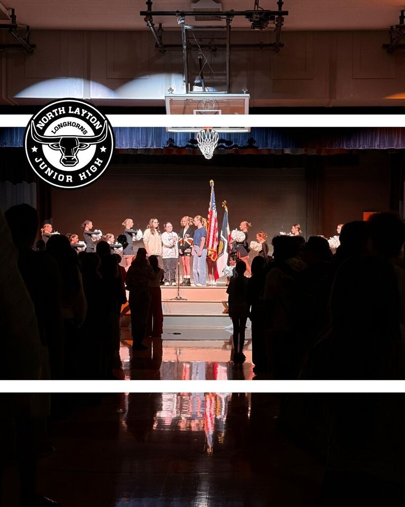 The cheerleaders stand on stage holding the American Flag, while choir students sing the national anthem 
