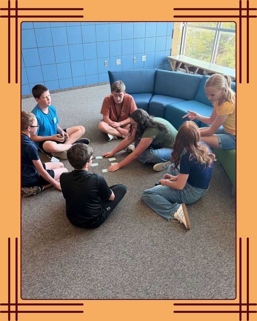 One group of West Point Junior High students from National Junior Honors Society at the opening social; they have a card game spread on the floor, and are huddled around the cards. They are having fun and getting to know one another.