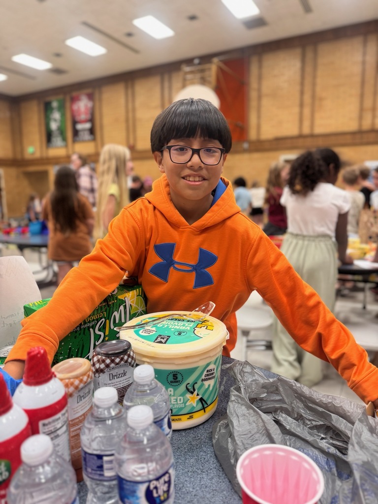 4th grader in orange hoodie and wearing glasses. He is standing in the cafeteria for his trading post.