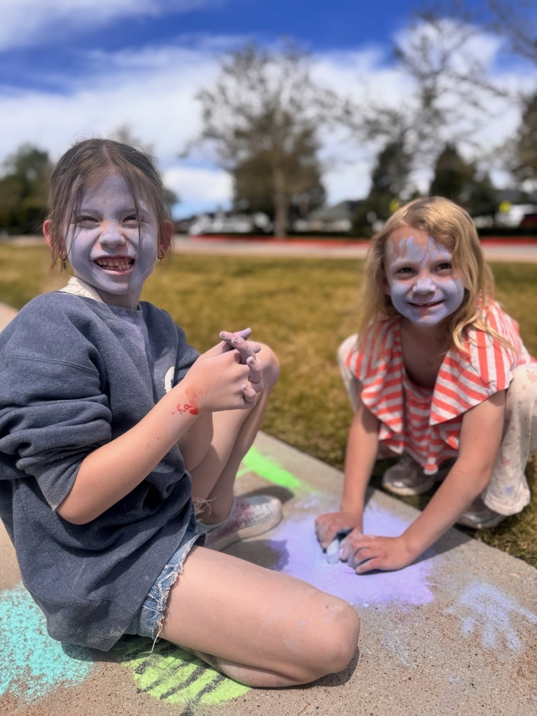 1st graders with sidewalk chalk on their faces drawing on the sidewalk