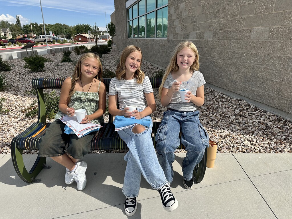 three girls eating snow cones on a bench