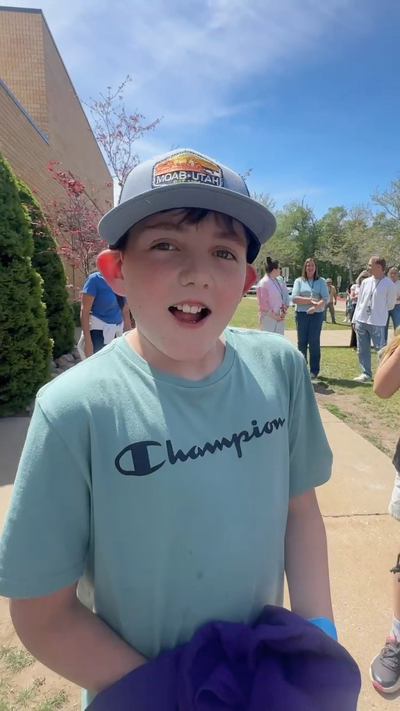 4th grade boy in gray ball cap and blue shirt standing in front of elementary school