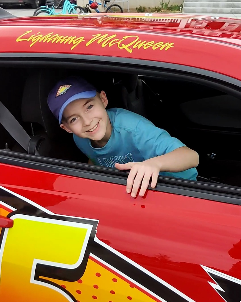 A student in a hat smiles while inside a race car.