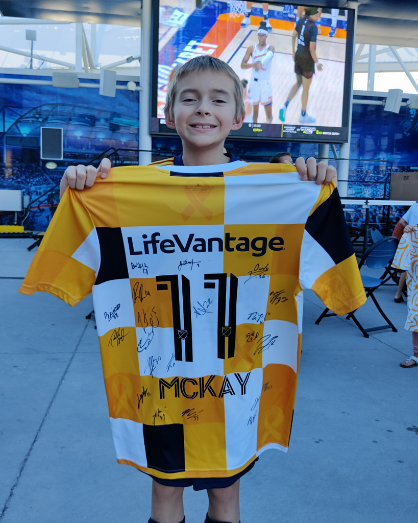 A student smiles as they hold up a yellow, black and white checked jersey that says LiveVantage 11 McKay.