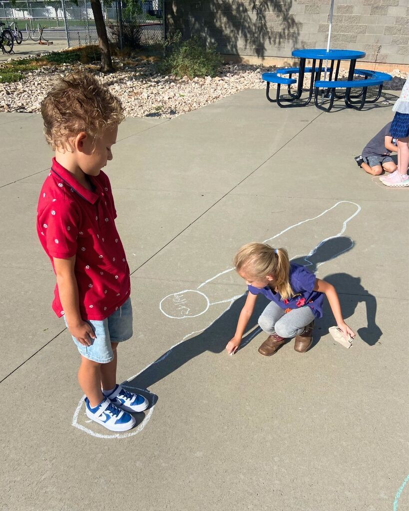 First-grade students trace and observe their shadows outside during a science investigation.