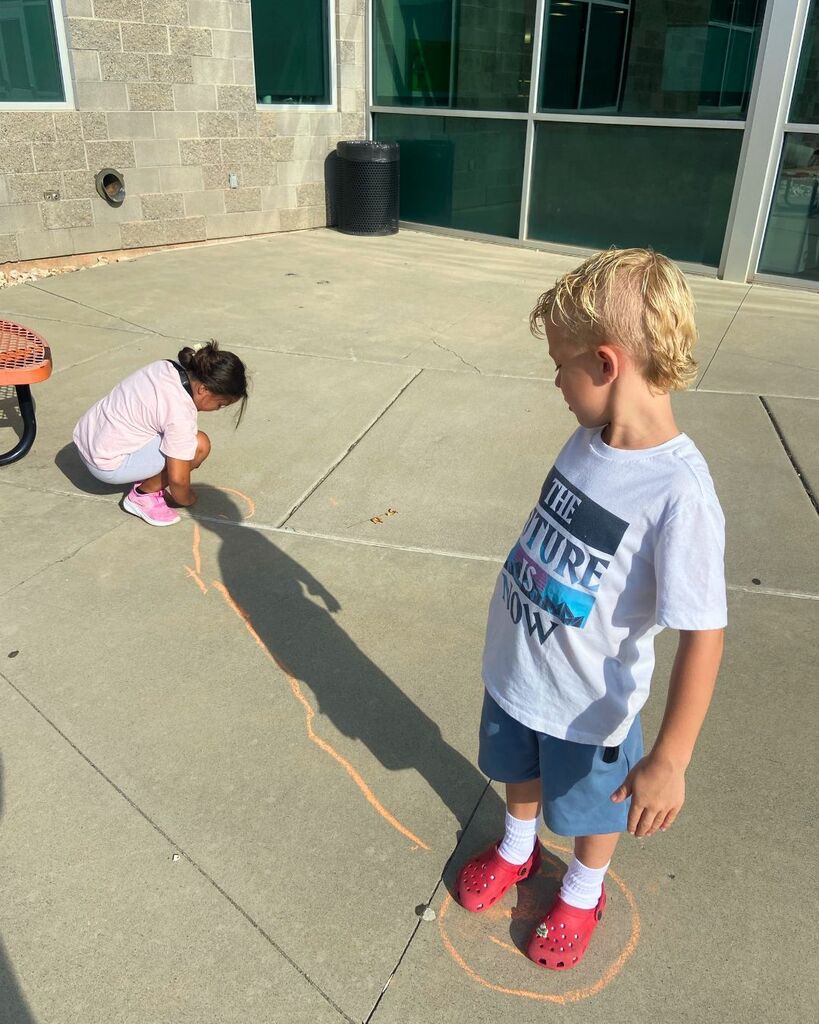 First-grade students trace and observe their shadows outside during a science investigation.