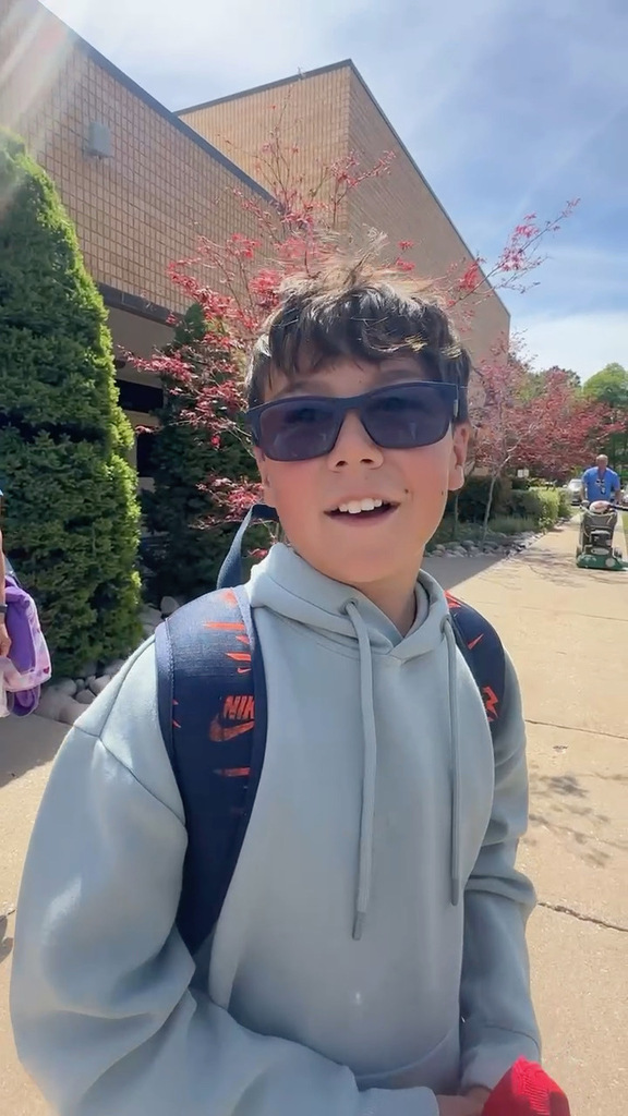 Student in glasses and gray hoodie standing in front of school.