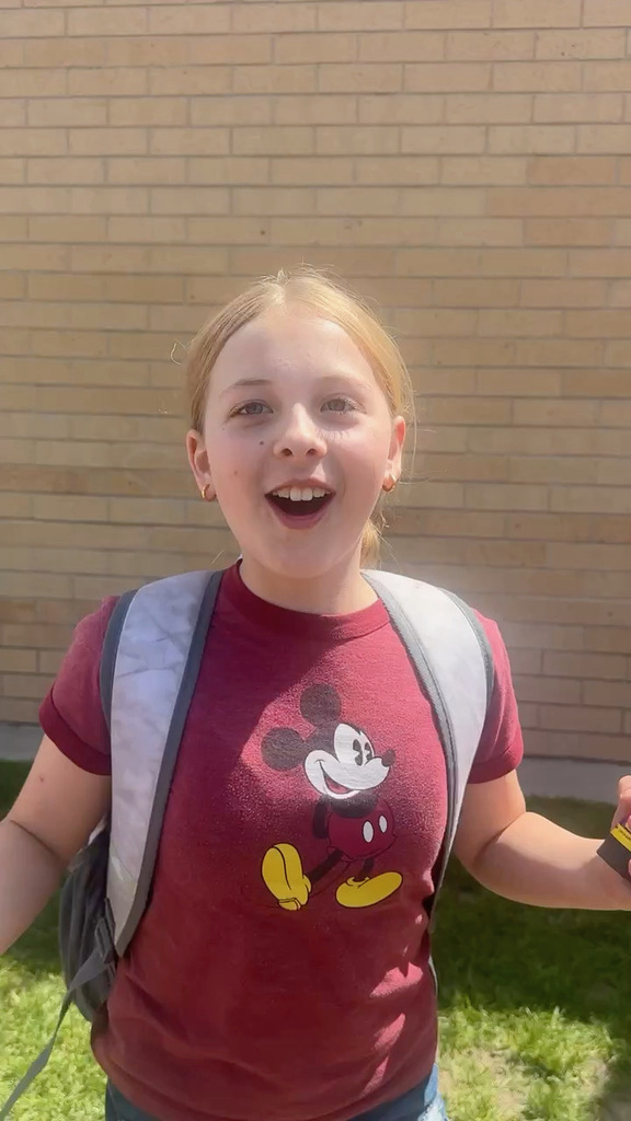 Female student in red shirt with Mickey Mouse on the front excited in front of elementary school