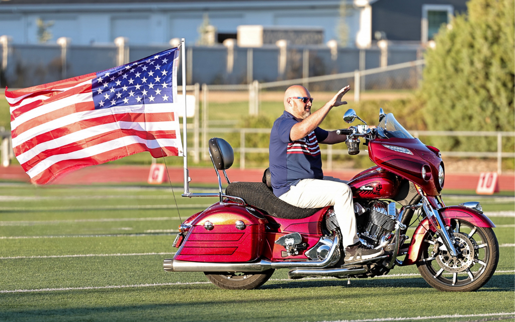Syracuse High Principal Brad Chapple rides his motorcycle with an American Flag on the back.