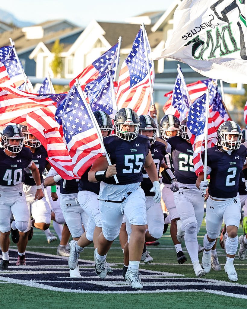 Syracuse High Football players run onto the field with flags.